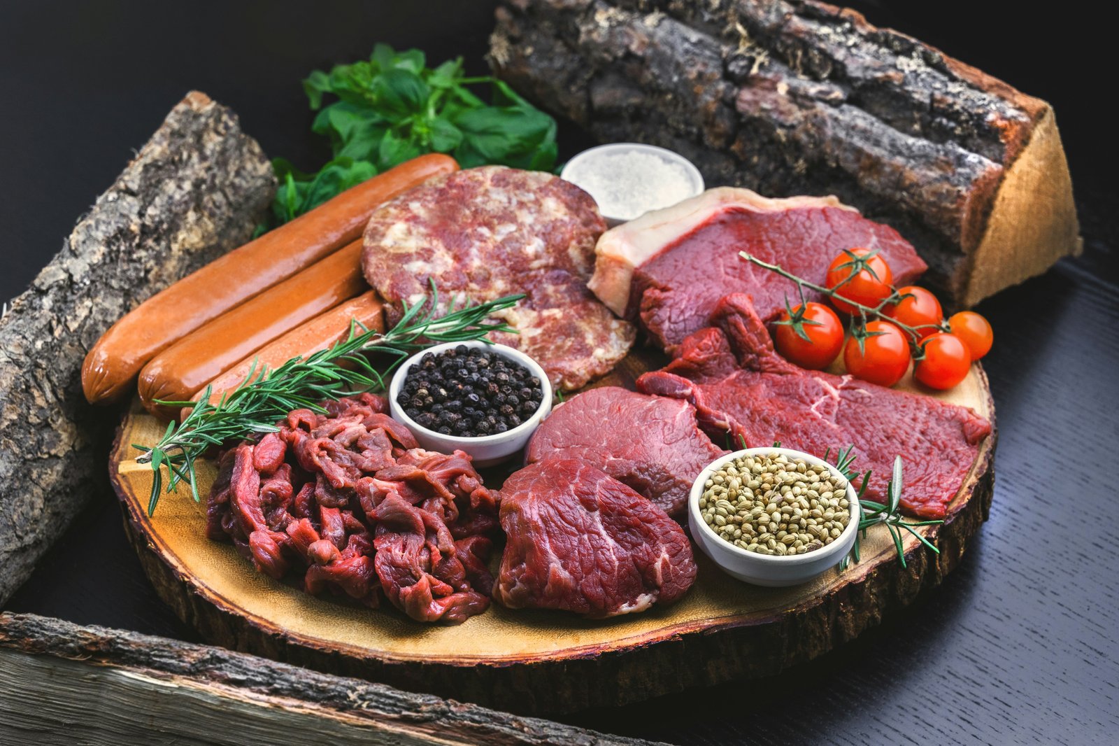 Fresh beef cuts and sausages on a wooden board with rosemary and spices